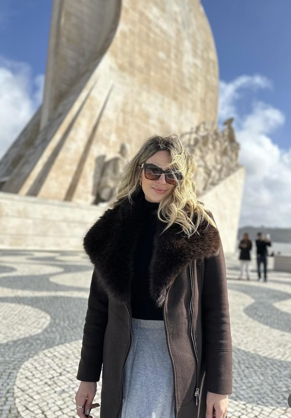 Núbia de casaco com gola de pelo diante do Padrão dos Descobrimentos, em Lisboa